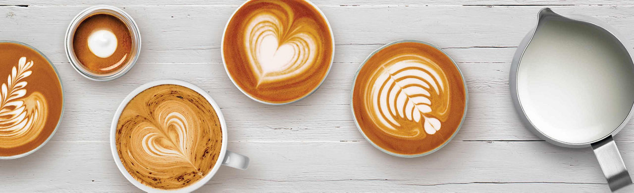 Various latte art with milk jug on bench