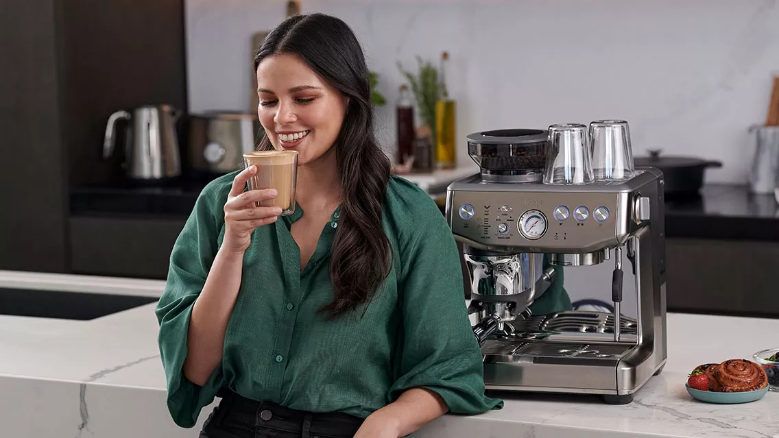 Woman holding a cup of coffee next to the machine.