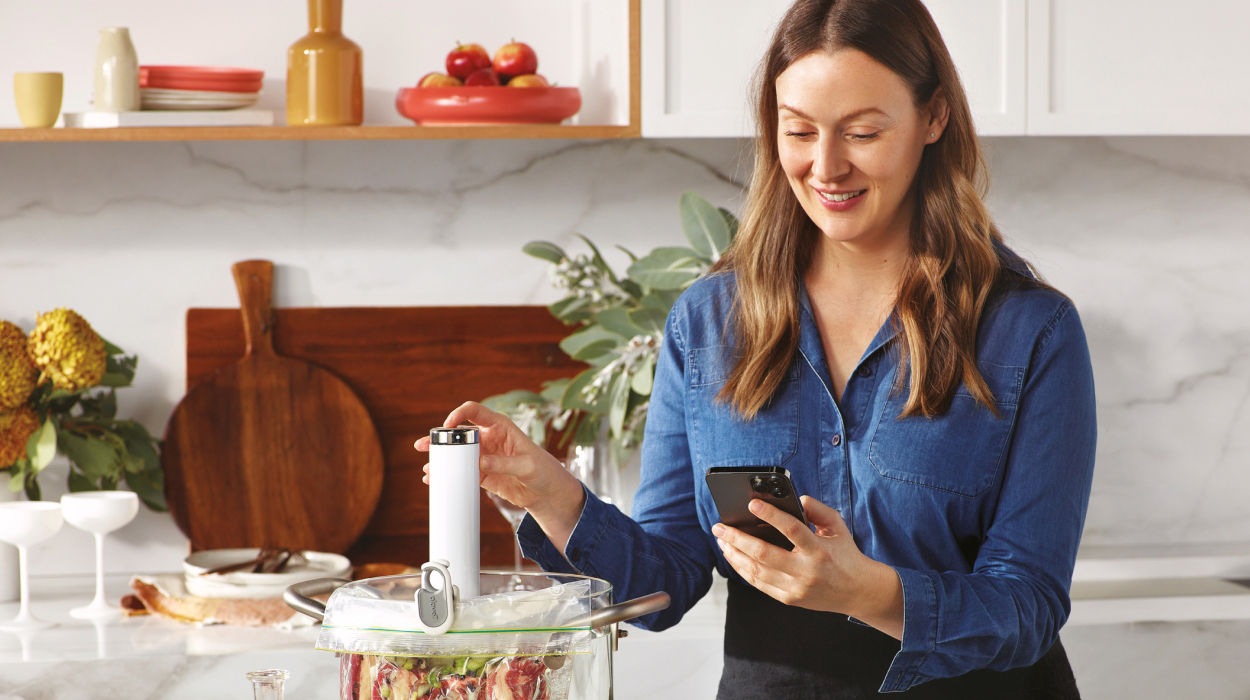 Woman looking at phone and touching the Joule Turbo Sous Vide