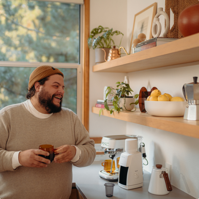 A man smiling next to a kitchen containing a Baratza coffee grinder and a Bambino espresso machine.