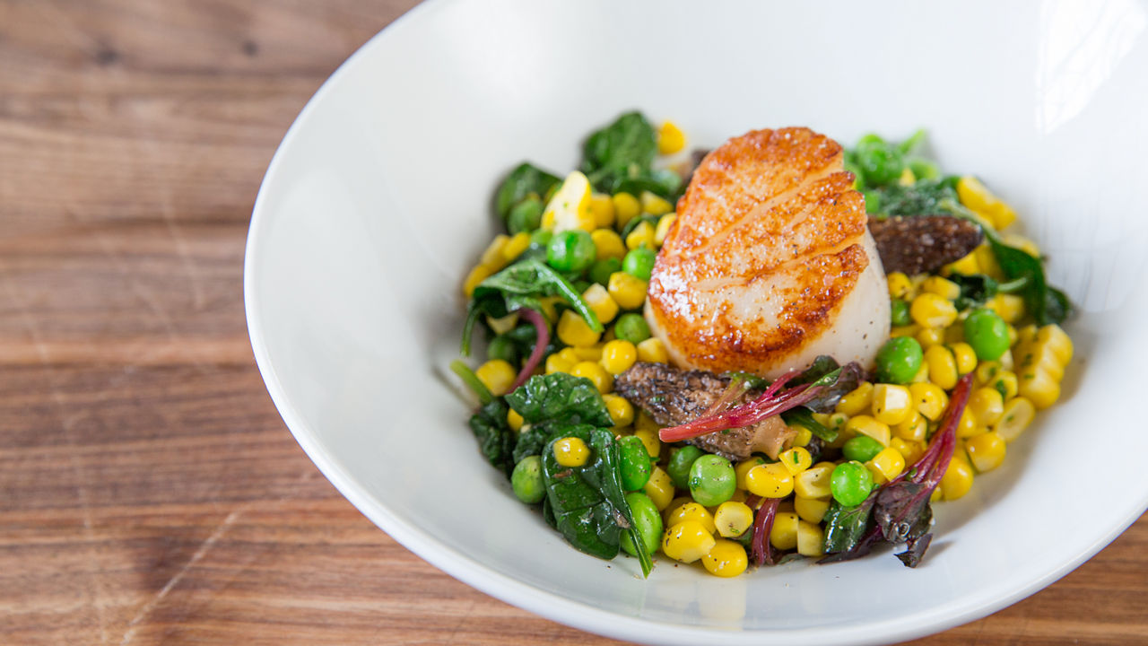 A seared scallop on a bed of peas, corn, and vegetable. 